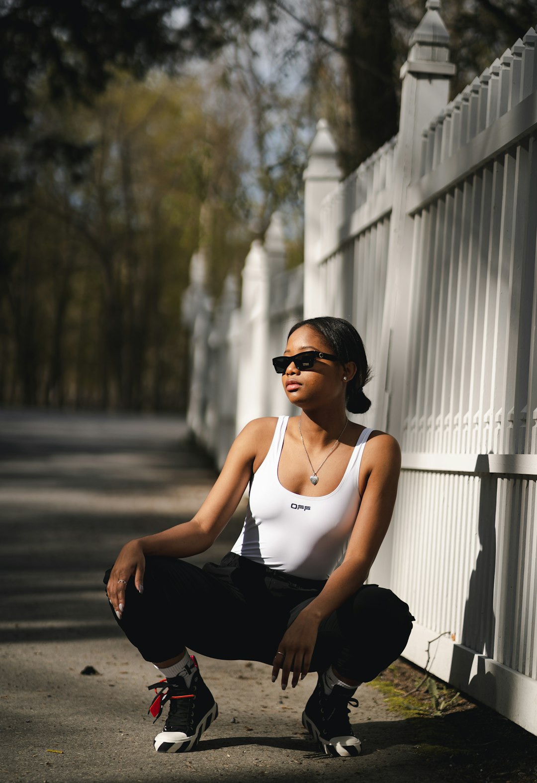 woman in white tank top and black pants wearing black sunglasses sitting on sidewalk during daytime