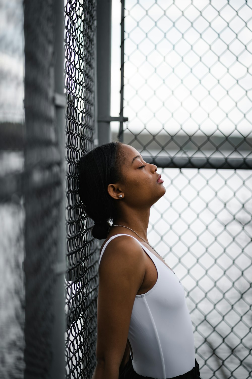 woman in white tank top leaning on chain link fence