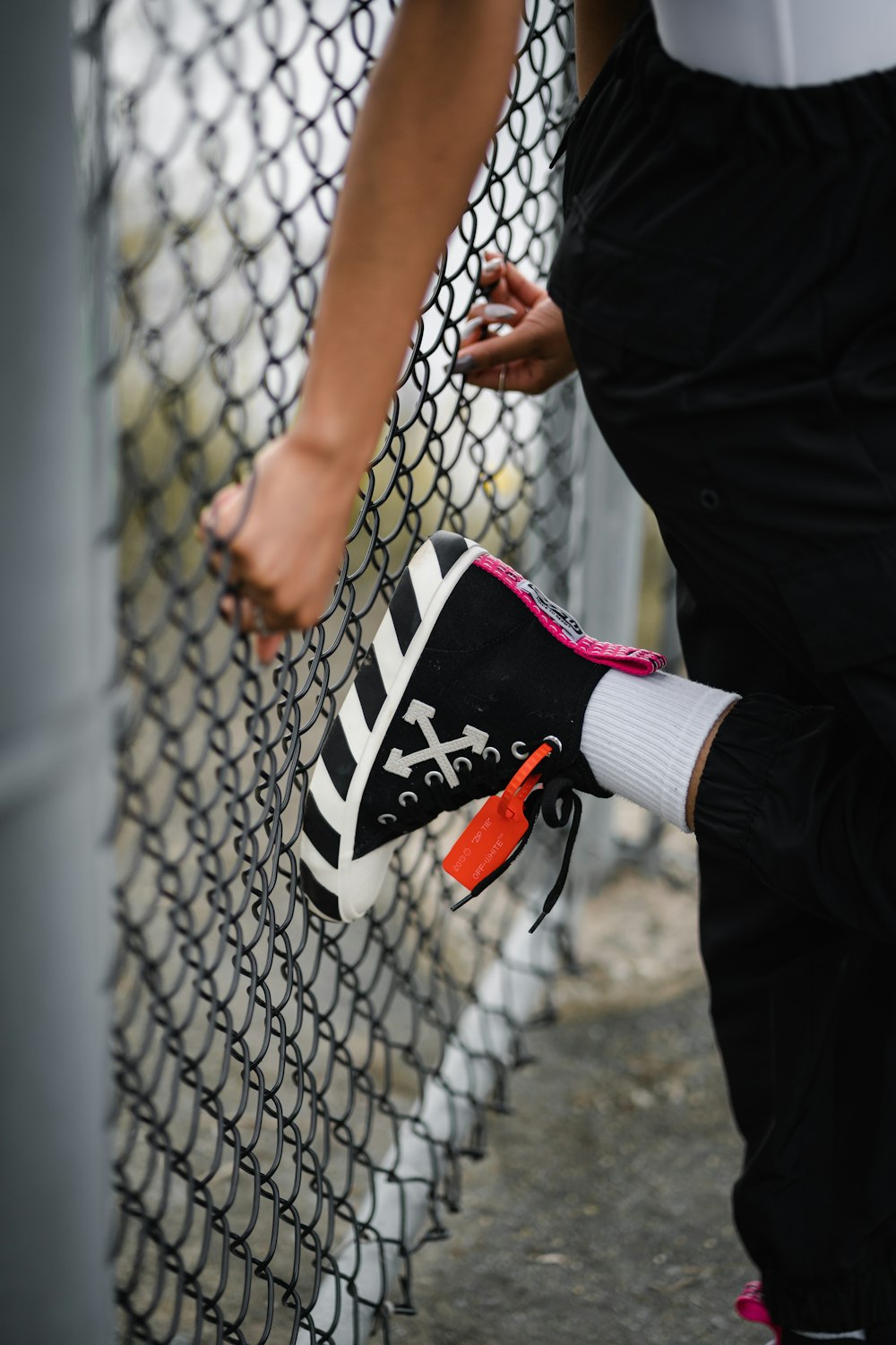 person in black pants and black and white nike sneakers standing beside gray chain link fence