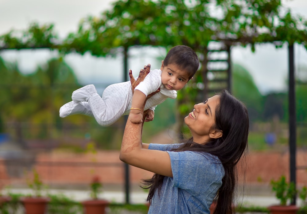 woman in blue denim button up shirt carrying girl in white long sleeve shirt during daytime