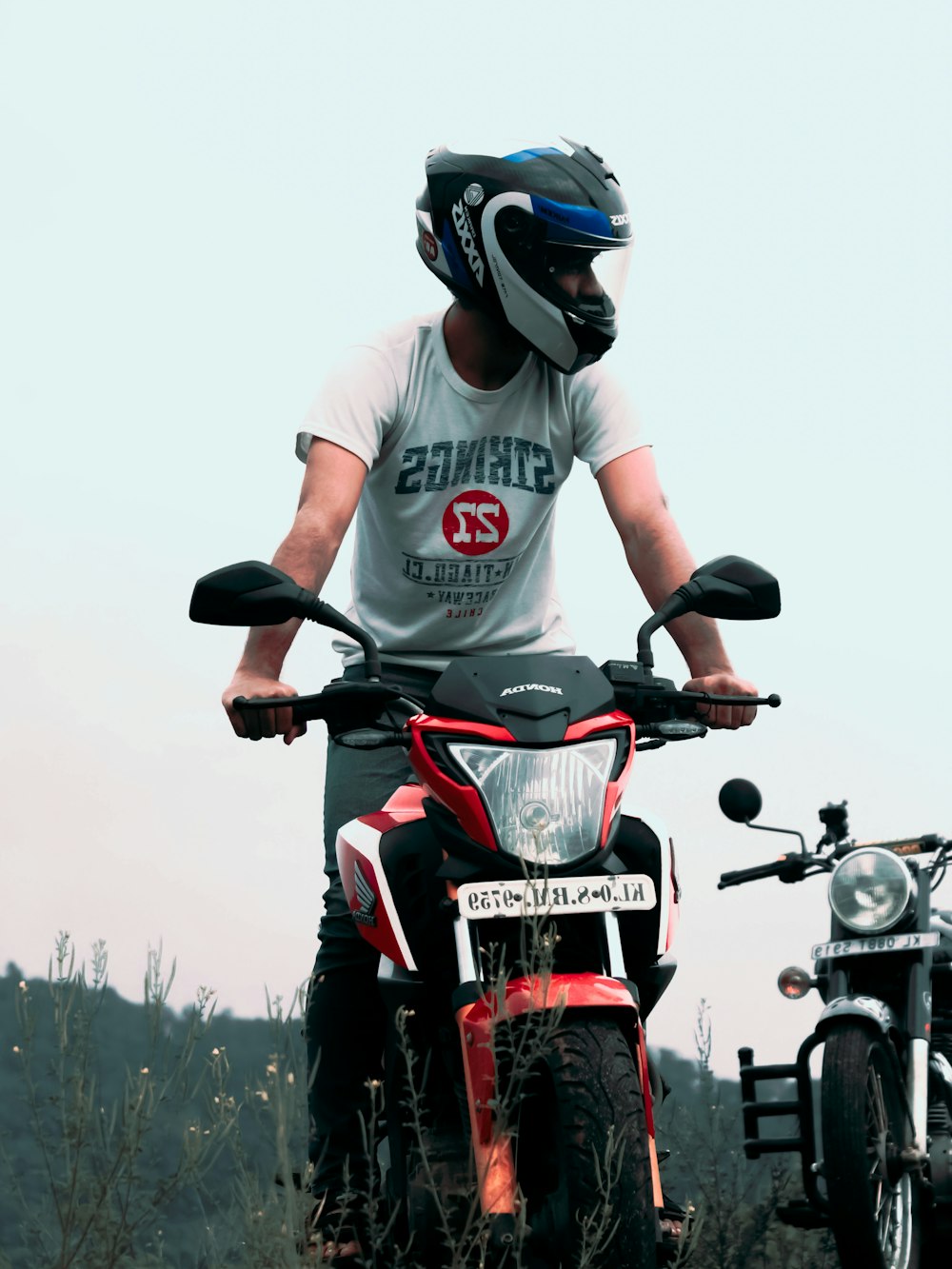uomo in t-shirt girocollo bianca e rossa in sella a una moto rossa e nera