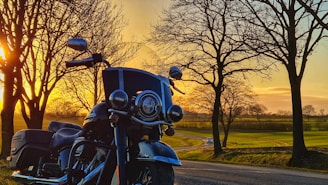 A vintage motorcycle parked on a scenic country road during sunset.