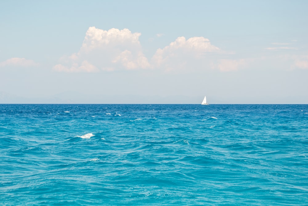 white sailboat on blue sea under white clouds during daytime