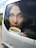 A large decal on a vehicle window features the face of a woman with dark hair holding a white mug filled with what appears to be coffee or a hot beverage. The reflection in the glass shows some surrounding scenery including green grass and a cloudy sky.