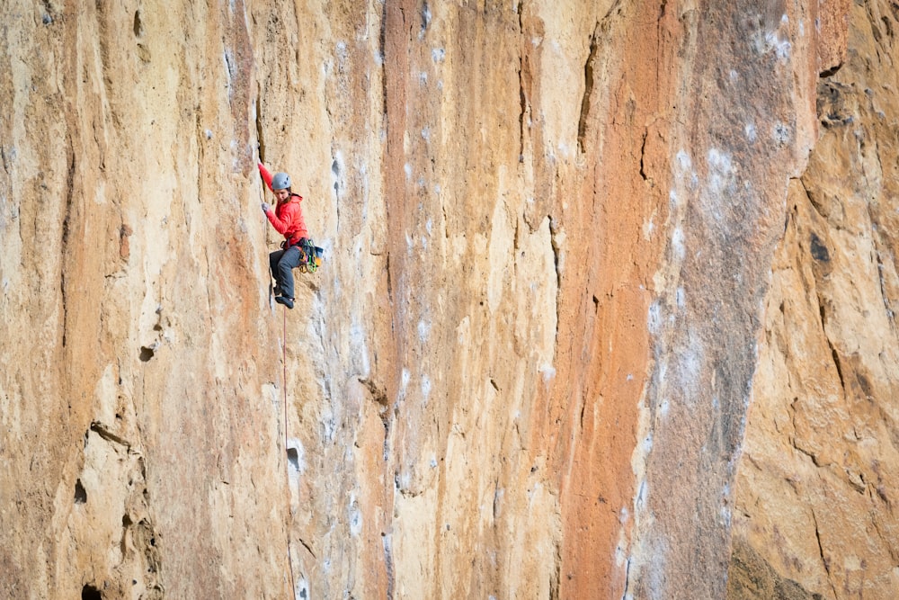 woman in red jacket and black pants climbing on brown wall