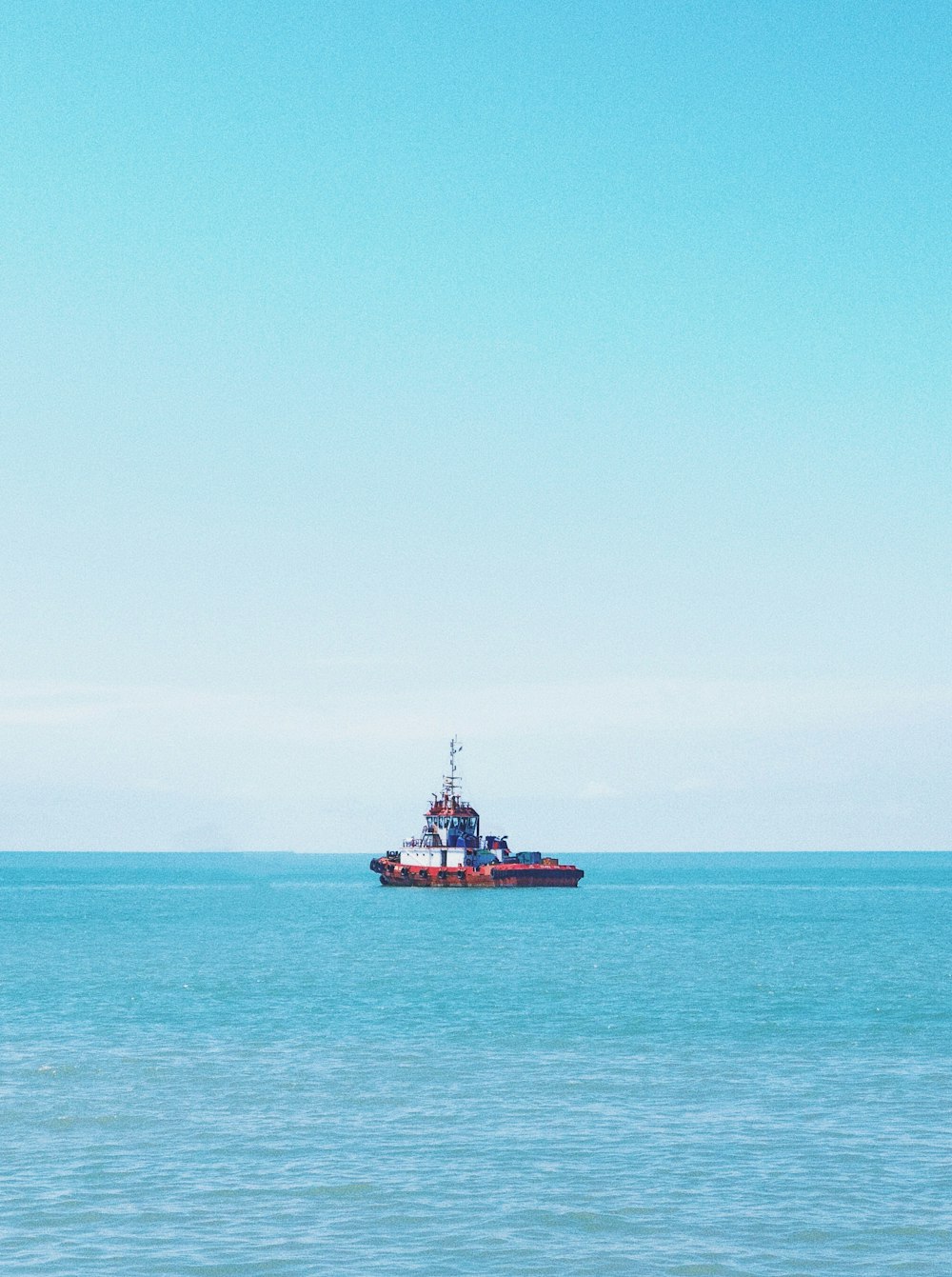 red and white ship on sea under blue sky during daytime