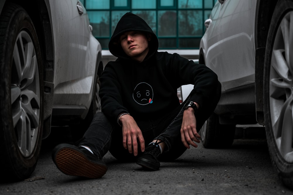 man in black hoodie and black pants sitting on gray concrete floor