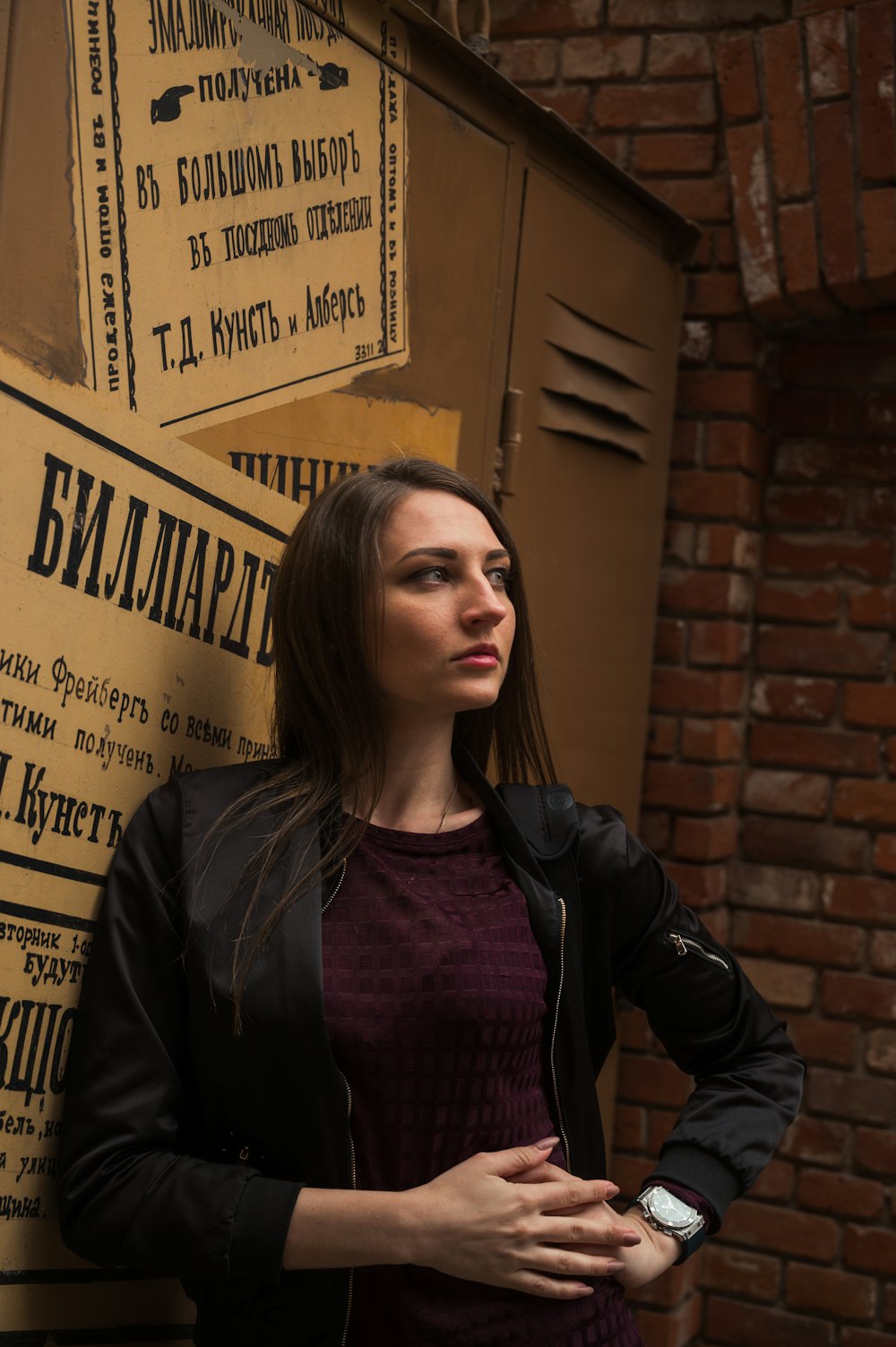woman in black leather jacket standing beside brown wall