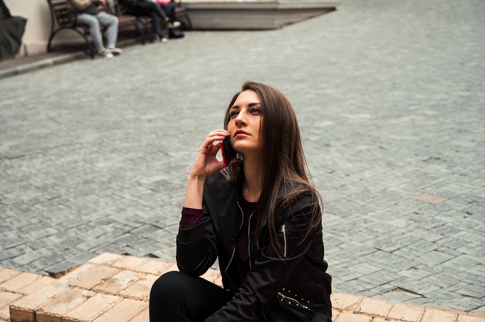 woman in black leather jacket sitting on brown brick floor during daytime
