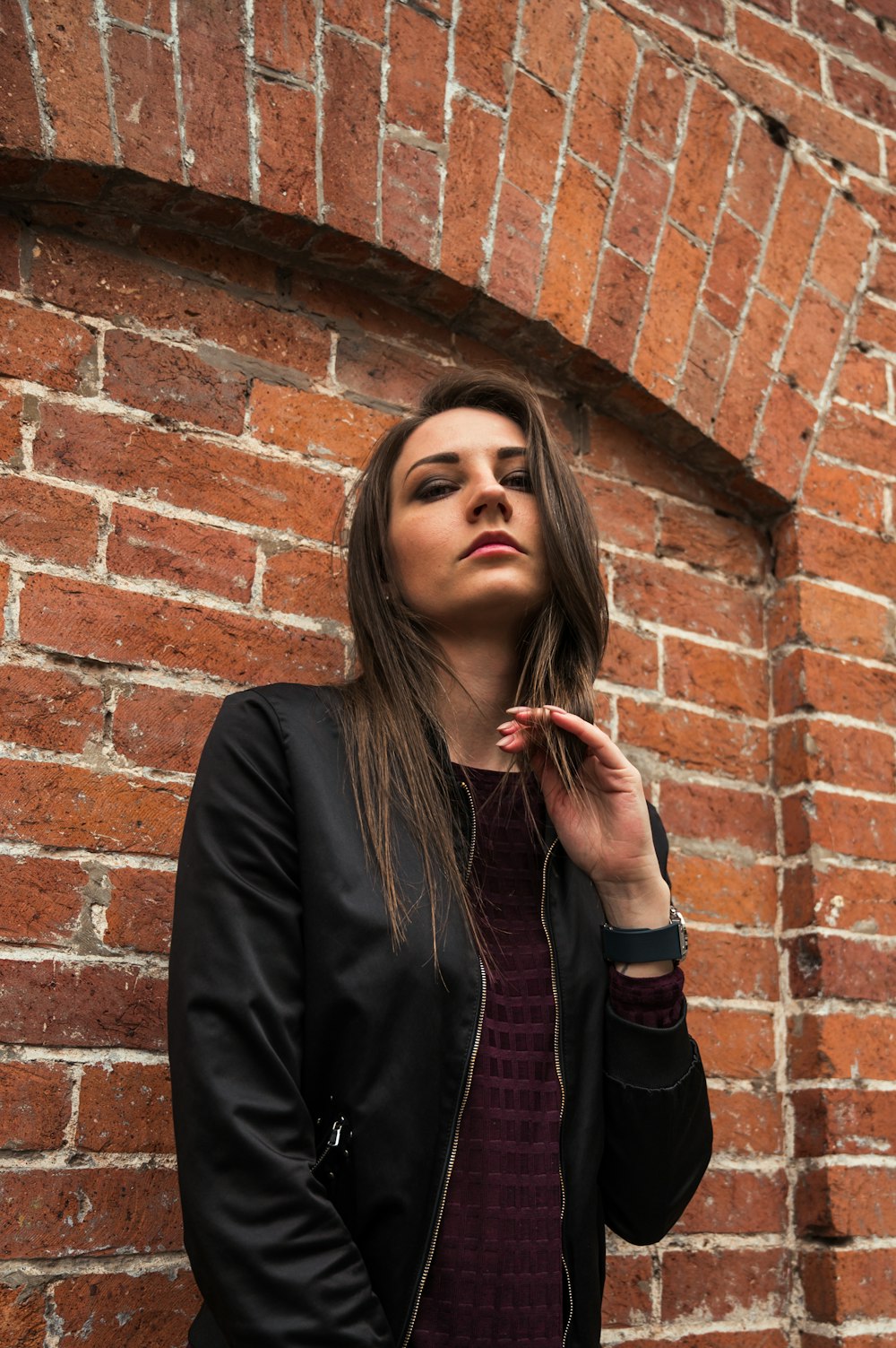 woman in black jacket standing beside brown brick wall