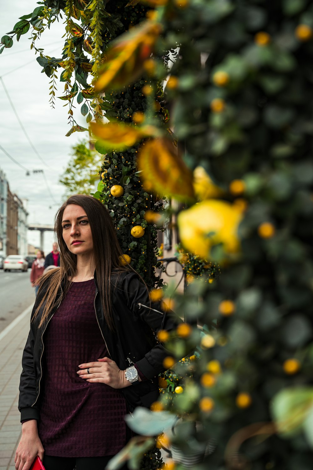 woman in black leather jacket standing beside yellow leaves during daytime