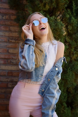 A candid shot of a fashion blogger laughing while adjusting her oversized sunglasses in natural light.