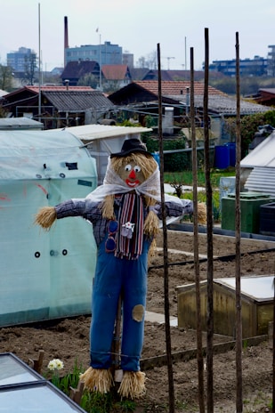 A kid-friendly scarecrow with a big smile standing guard by the garage door, wearing a colorful hat.