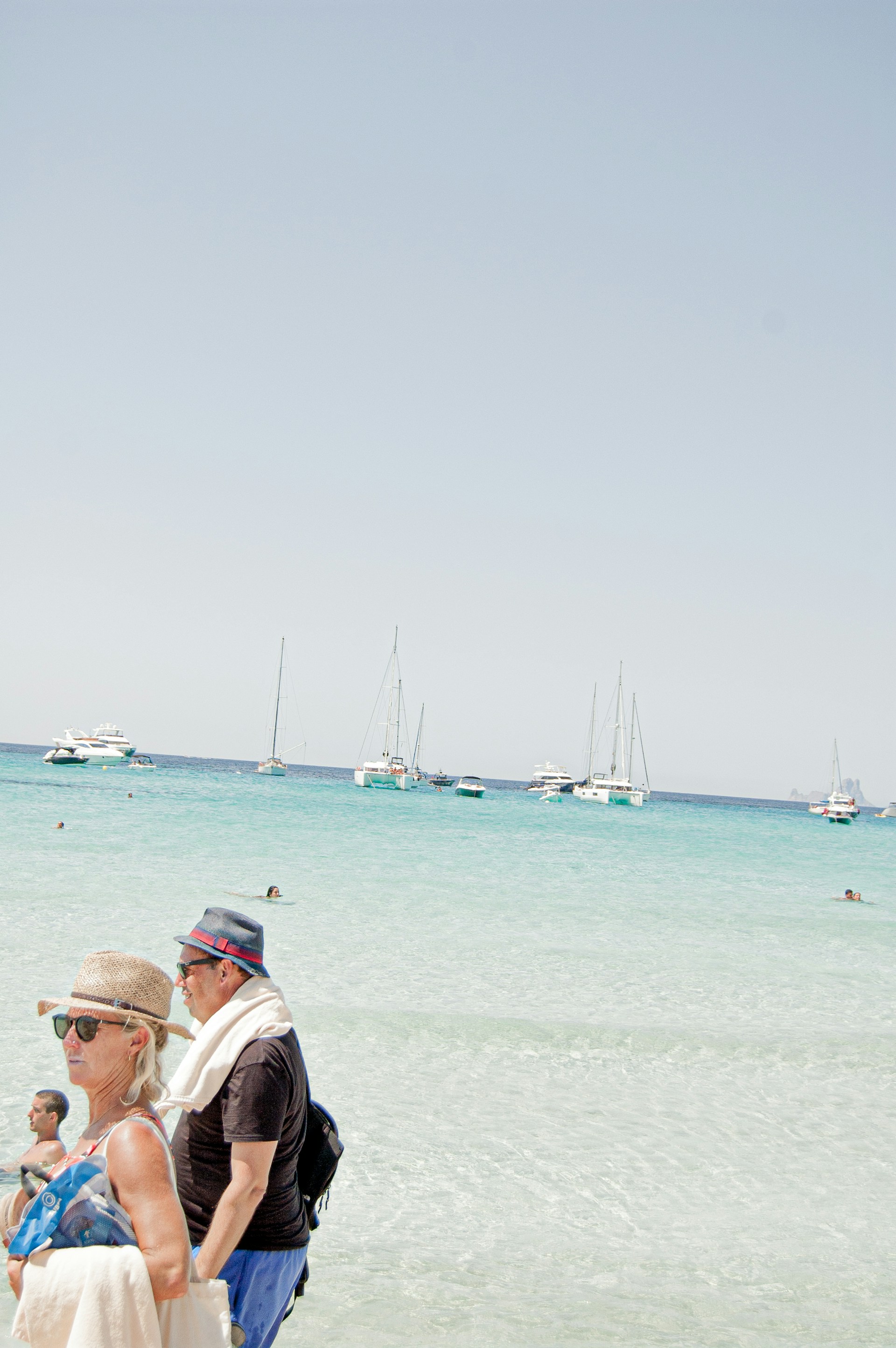 A bright, sunny day in Didim with colorful sailboats gliding over the clear blue Aegean Sea near the coastline.