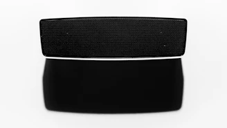 Close-up of a bold black and white wireless speaker with sharp edges glowing softly in a dark room.