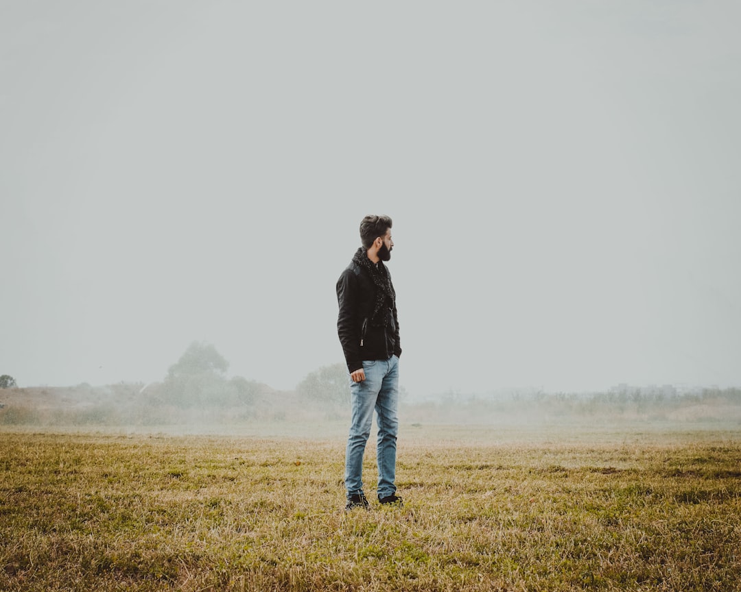 man in black jacket and blue denim jeans standing on green grass field during daytime