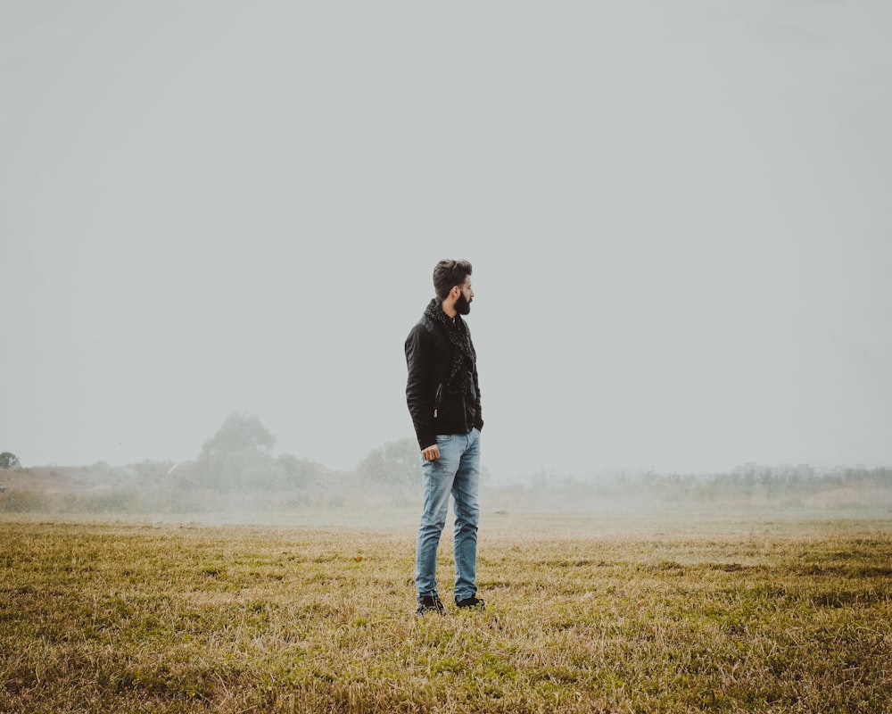 man in black jacket and blue denim jeans standing on green grass field during daytime