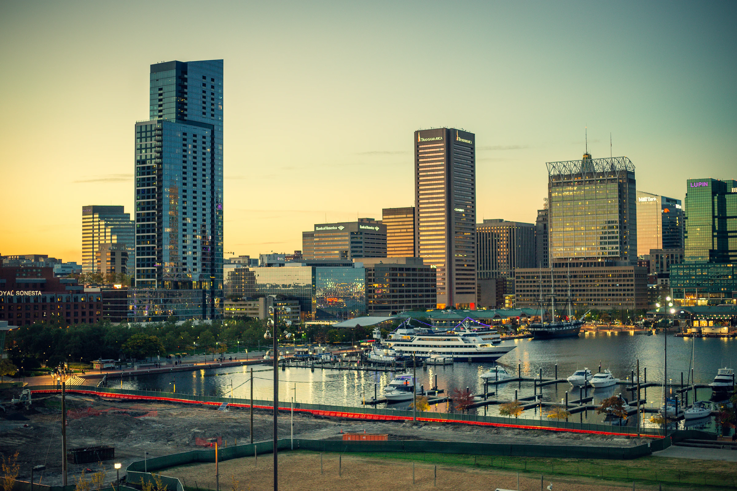 The Baltimore Inner Harbor skyline lit up at dusk, with boats moored along the waterfront