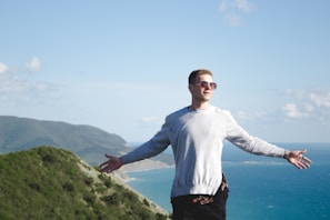 man in white long sleeve shirt standing on green mountain during daytime