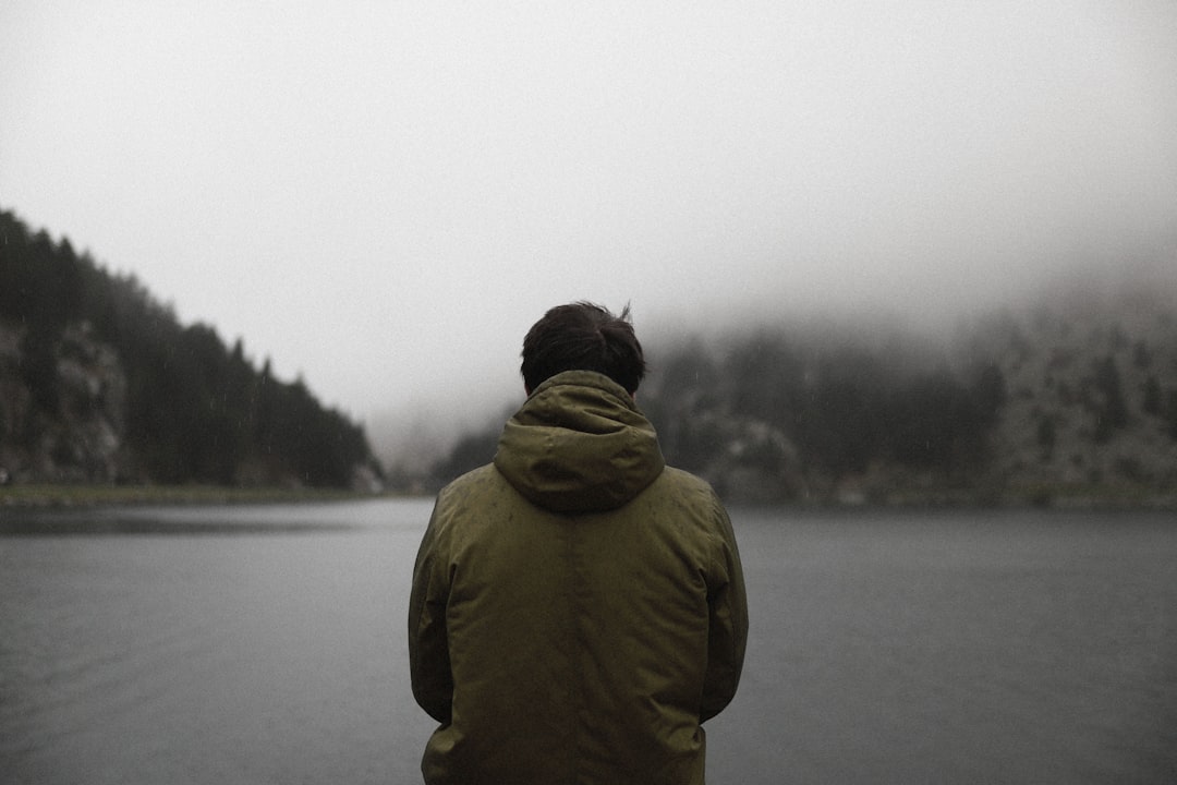 person in green hoodie standing near body of water during daytime