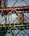 Rusty metallic structure composed of various intersecting beams and frames, possibly part of an industrial site or construction equipment. The metal shows signs of aging and corrosion, with patches of rust and faded paint. The background is a clear blue sky, providing a stark contrast to the aged metal.