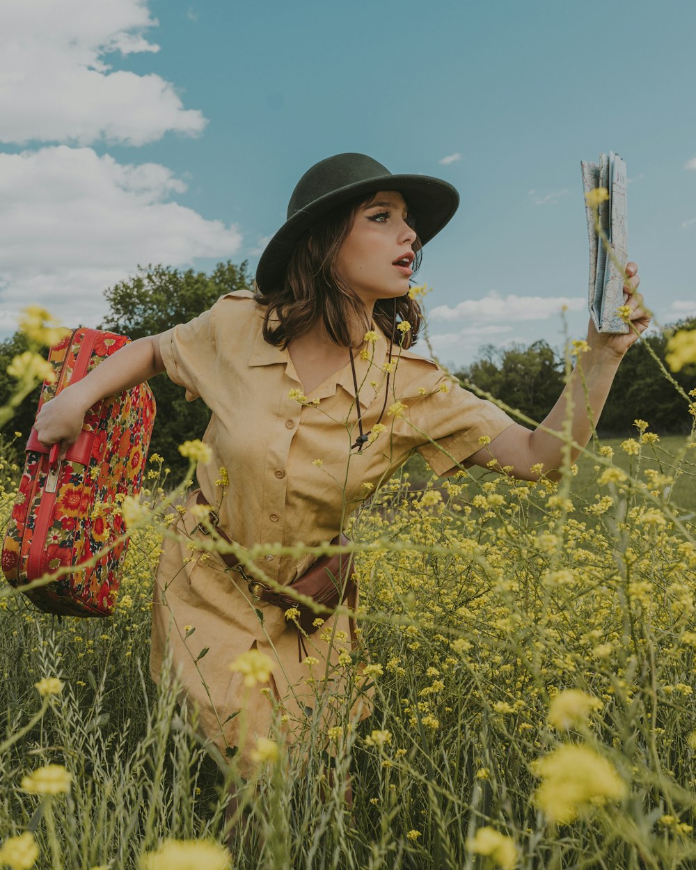 woman in brown dress and black hat standing on yellow flower field during daytime