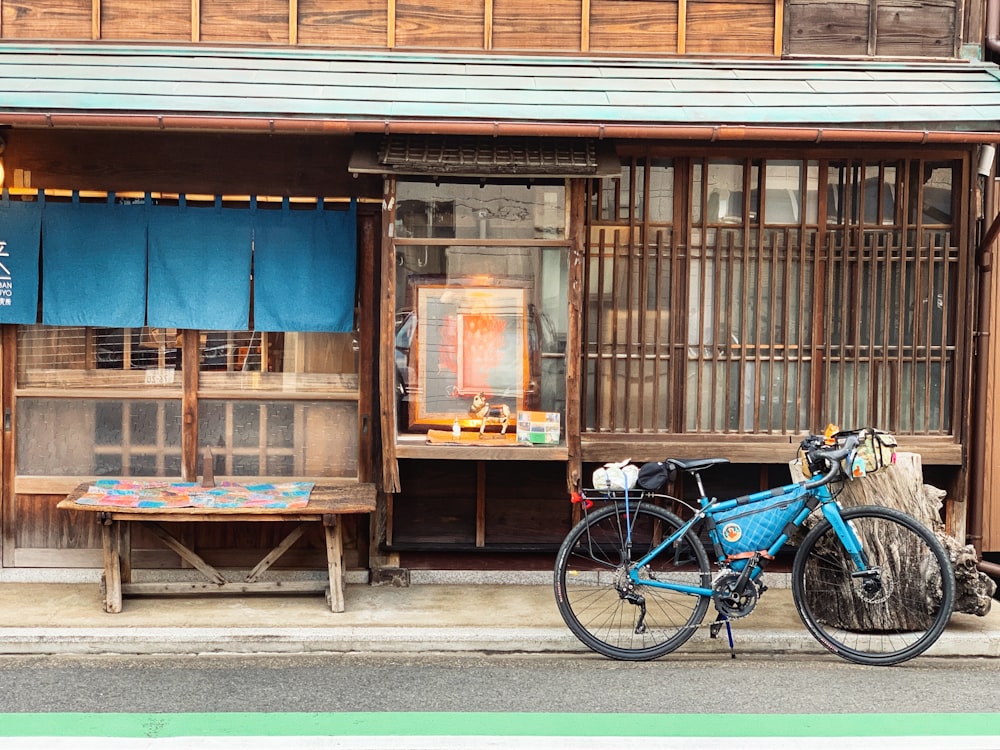 Bicicleta de ciudad azul estacionada junto a la casa de madera marrón durante el día