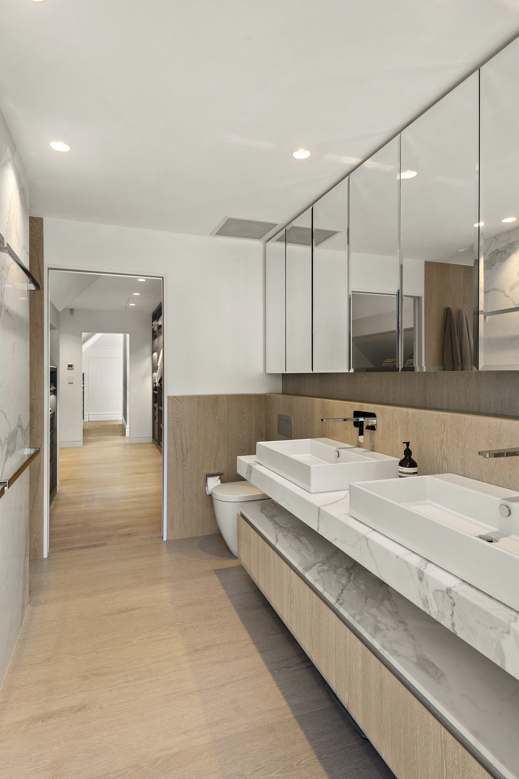 Contemporary bathroom with a long double vanity, two vessel basins, mirrored cabinetry, wood-look finishes and marble-look countertops.
