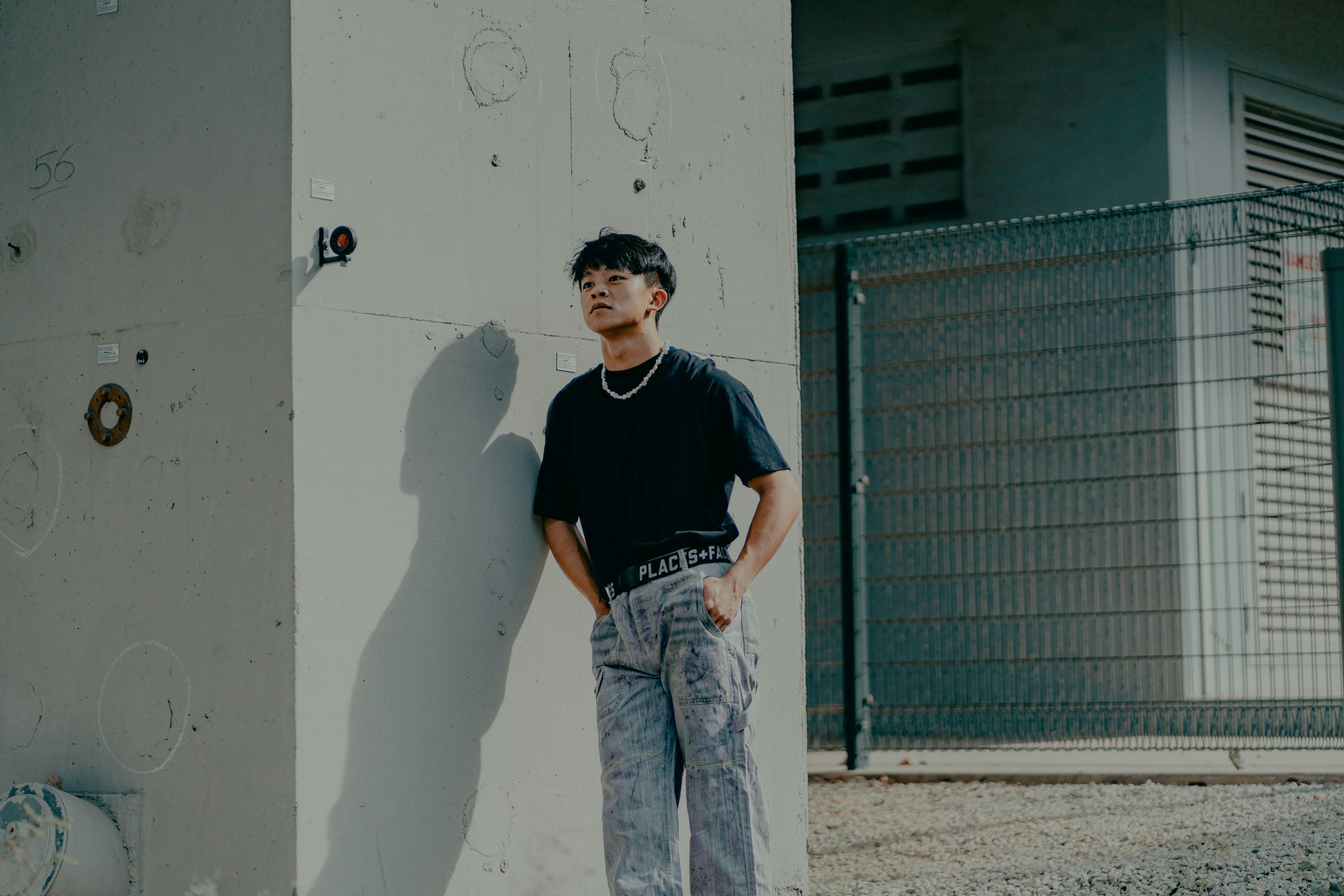 man in black crew neck t-shirt and blue denim jeans standing beside white wall during