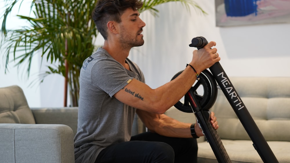 man in gray polo shirt and black pants sitting on black and white stationary bike