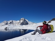 person in red jacket and white pants sitting on snow covered ground during daytime
