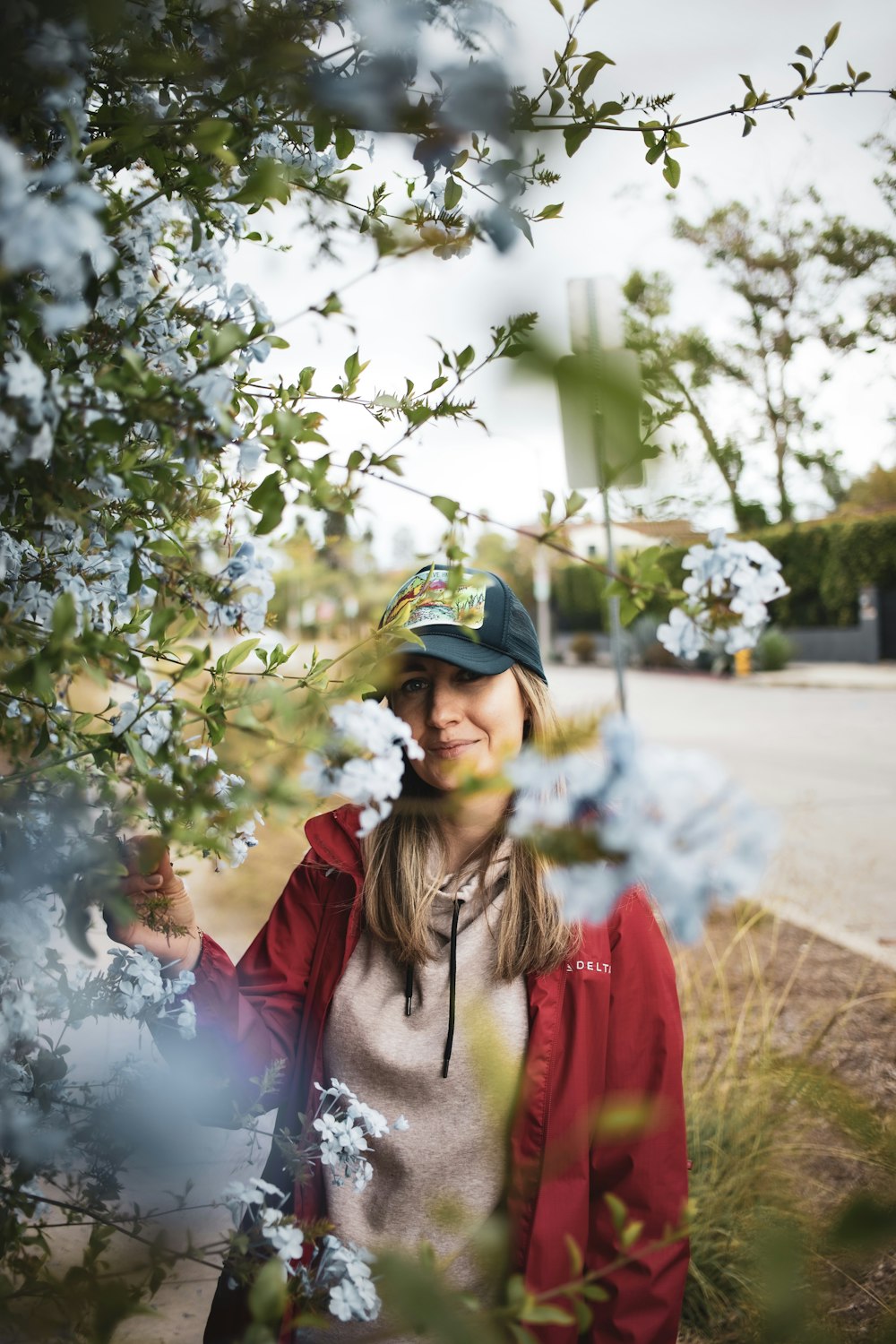 woman in red and white jacket standing near white flowers during daytime