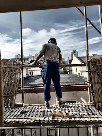 A construction worker reviewing blueprints on a building site with a city skyline in the background.