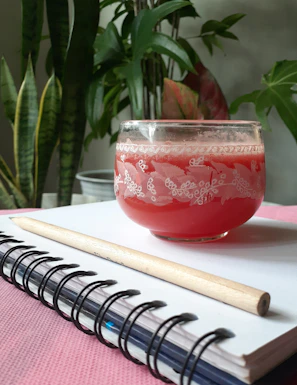 A sunny morning scene with a glass of fresh juice next to a notebook and a small plant.