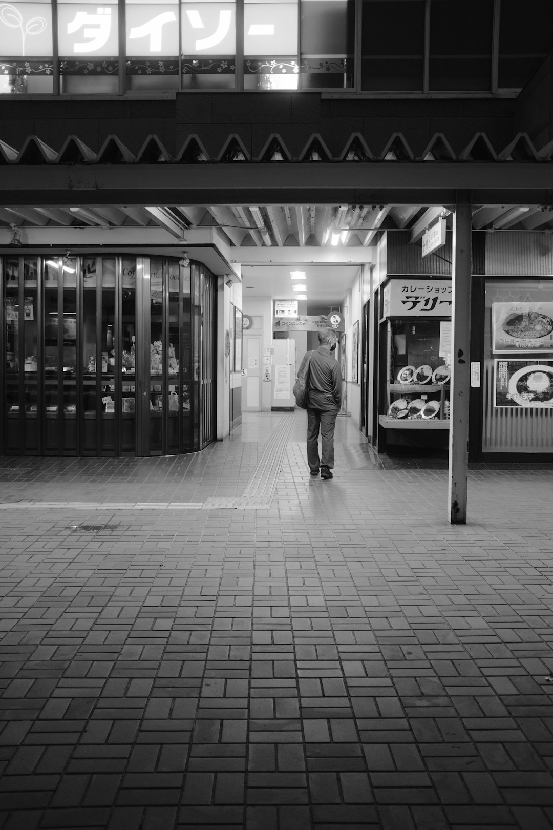 grayscale photo of man walking on sidewalk