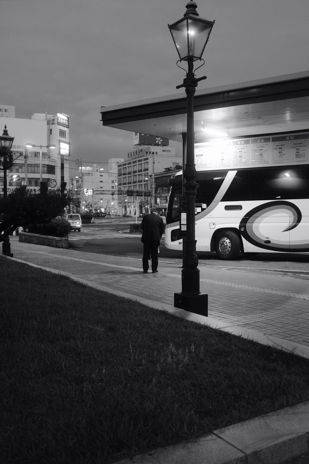 grayscale photo of man walking on sidewalk near building