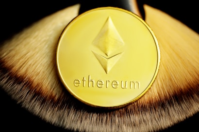 A gold coin with the word 'ethereum' and a geometric logo is placed on a textured surface that resembles a brush or fur. The focus is on the shiny details and the rich, warm tones of the coin.
