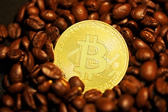 A shiny gold-colored Bitcoin coin is surrounded by dark roasted coffee beans.