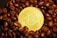 A shiny gold-colored Bitcoin coin is surrounded by dark roasted coffee beans.