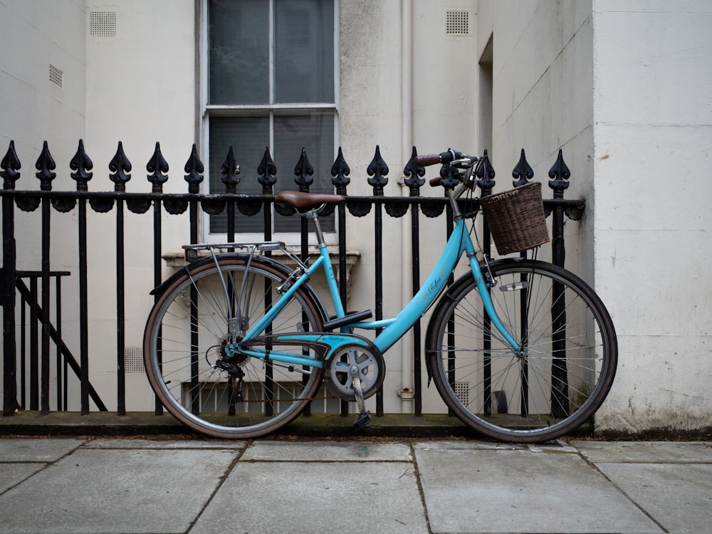 Bicicleta urbana azul y negra estacionada junto a la valla de metal negro