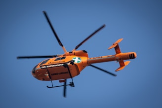 An ambulance helicopter landing on a hospital rooftop helipad under a clear blue sky.