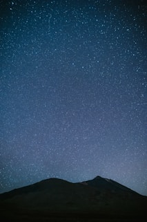A silhouette of a mountain range under a starry sky.