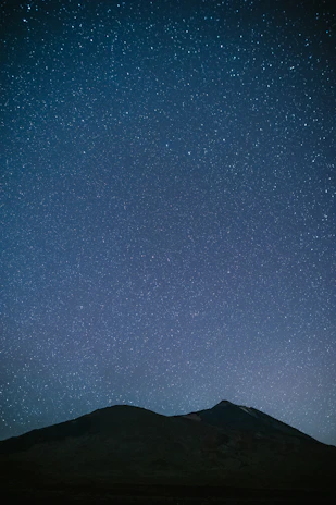 A panoramic shot of a mountain range under a clear night sky filled with stars.