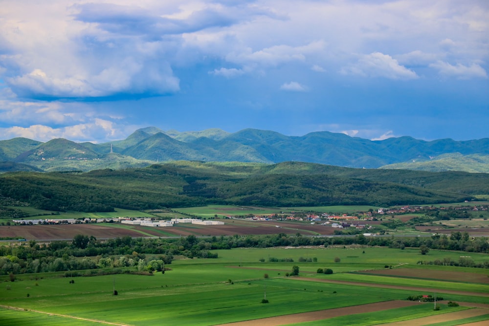 green grass field near mountain under blue sky during daytime