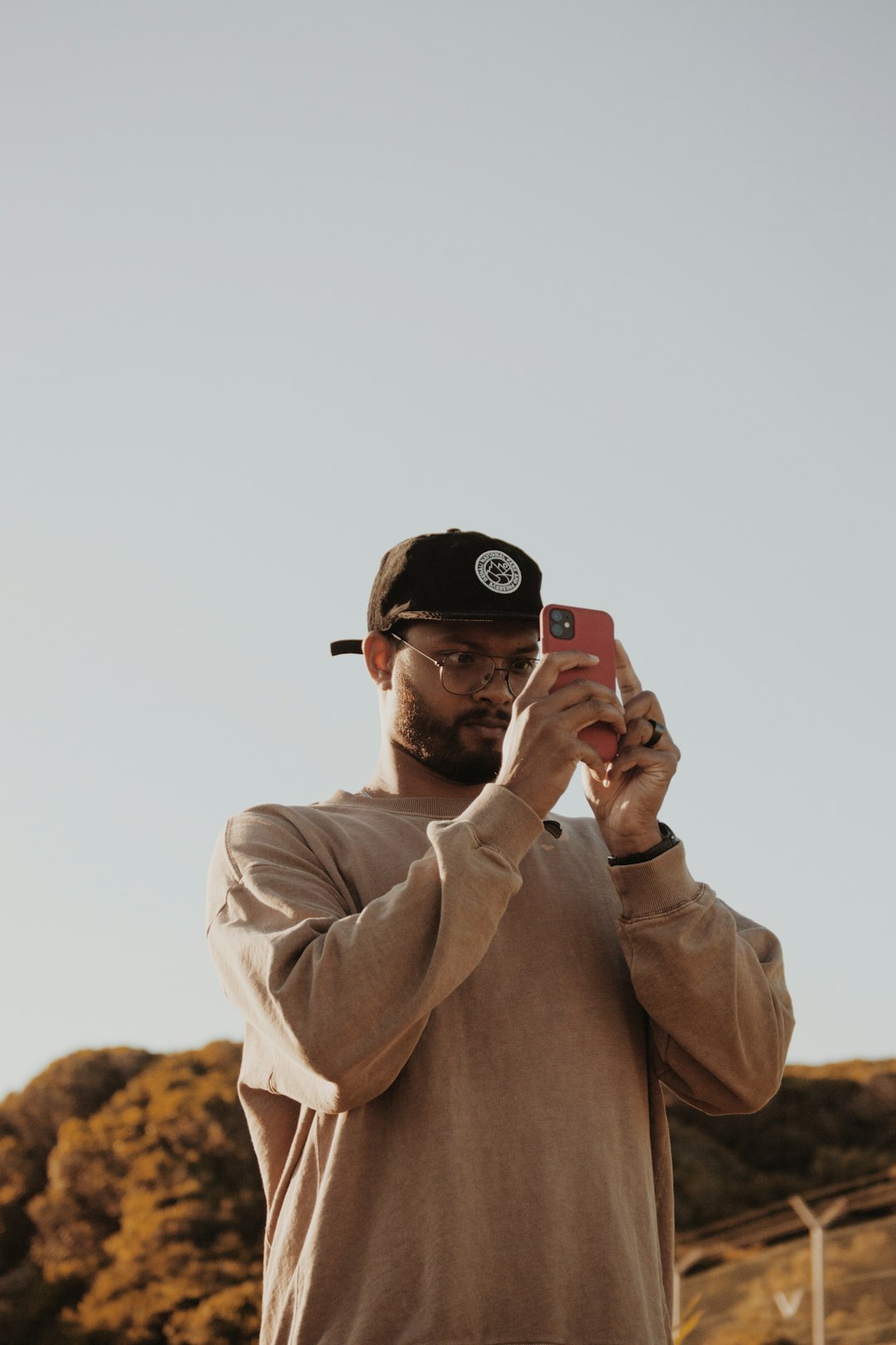 man in brown coat wearing black cap holding black smartphone