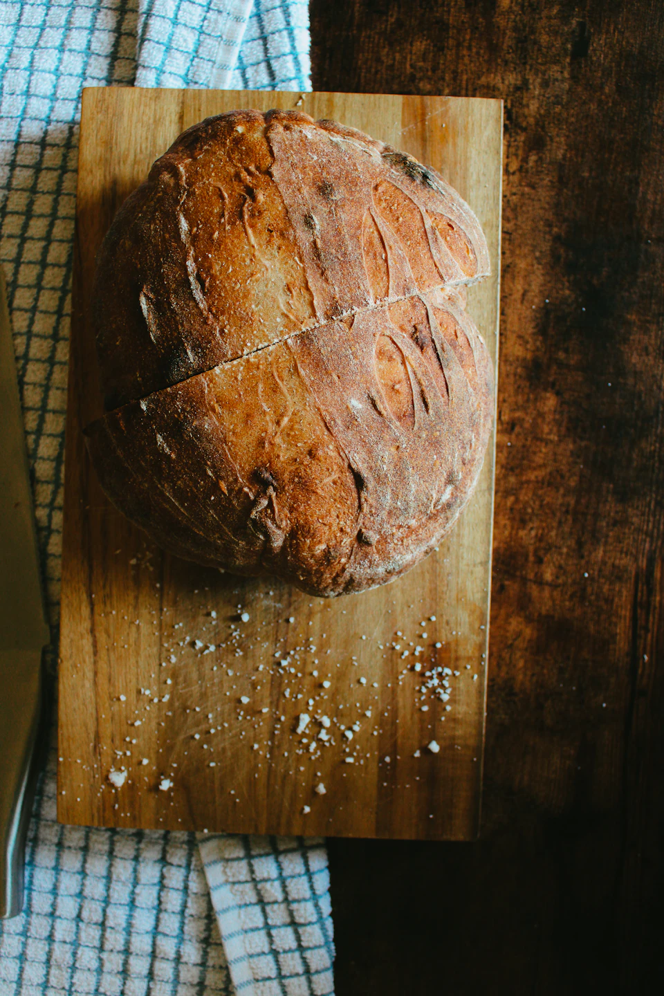 Freshly baked loaf of bread on wooden cutting board with golden crust and crumbs