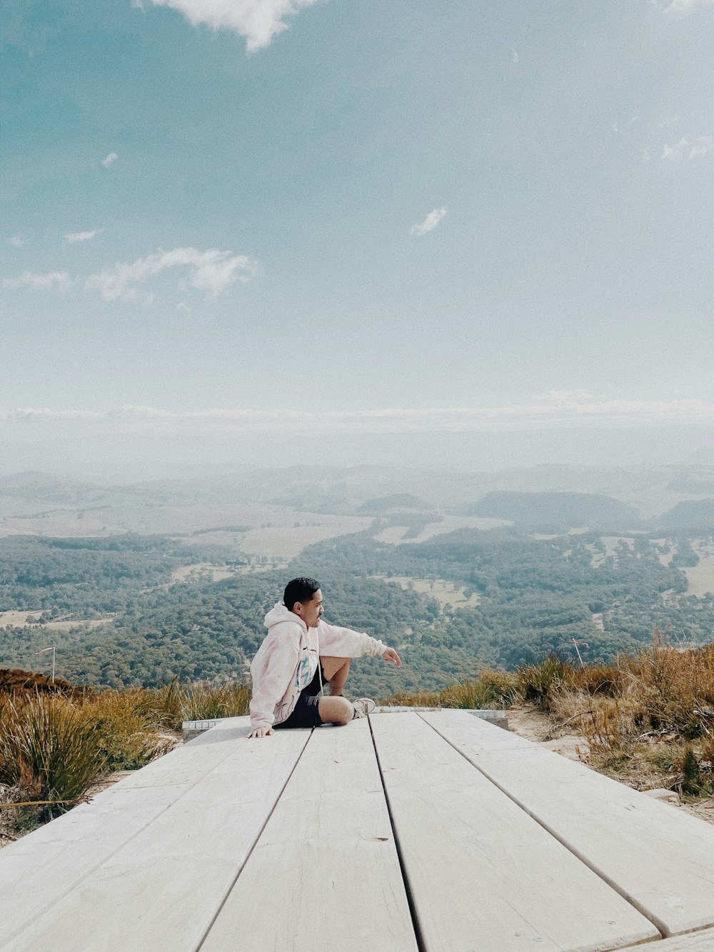 woman in white long sleeve shirt sitting on gray concrete pavement looking at the mountains during