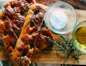 Warm, soft focaccia bread topped with rosemary and sea salt on a ceramic plate.