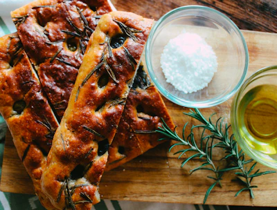 Warm, soft focaccia bread topped with rosemary and sea salt on a ceramic plate.