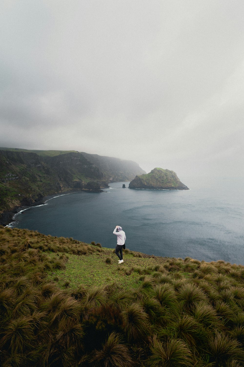 person in white shirt standing on green grass field near body of water during daytime